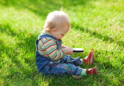 Kanak-kanak kecil sedang bermain dengan telefon bimbit di atas rumput hijai sewaktu pengamatan luar.