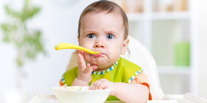 Bayi berusia 10 bulan sedang makan makanan padat finger food yang dipotong kecil.