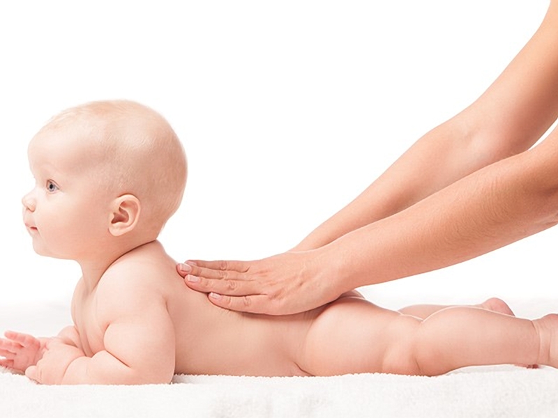 Ibu sedang mengurut bayi yang berbaring dengan lembut menggunakan minyak bayi