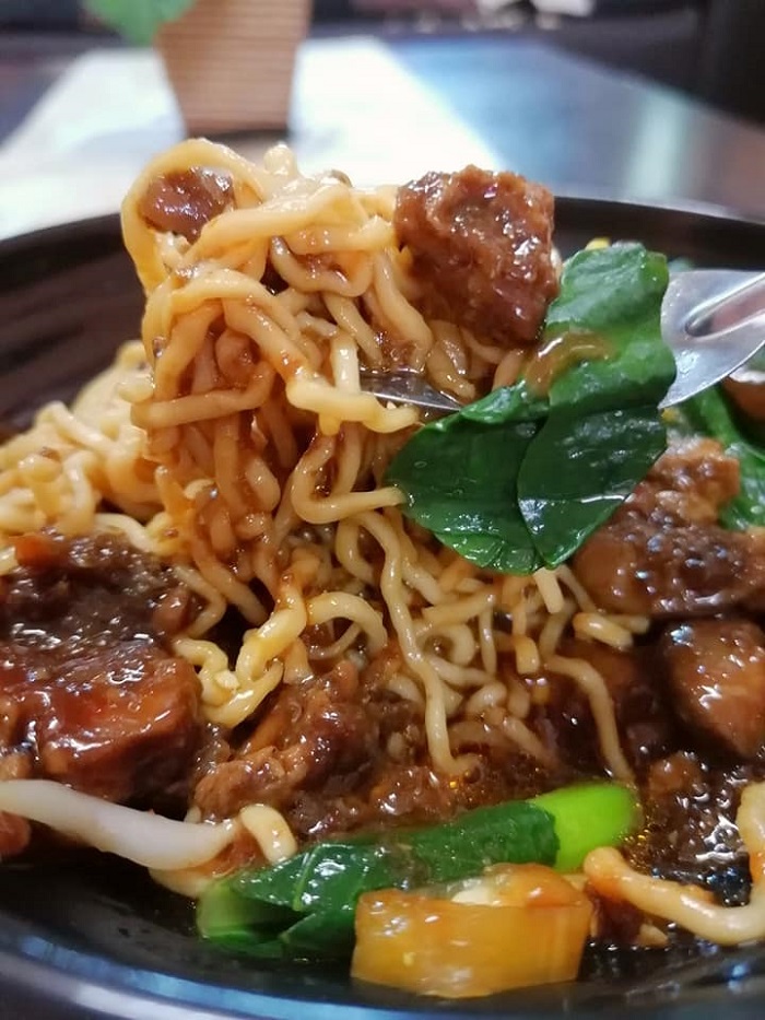 Semangkuk mie ayam Indonesia dengan kuah kicap pekat, ayam semur dan sawi.