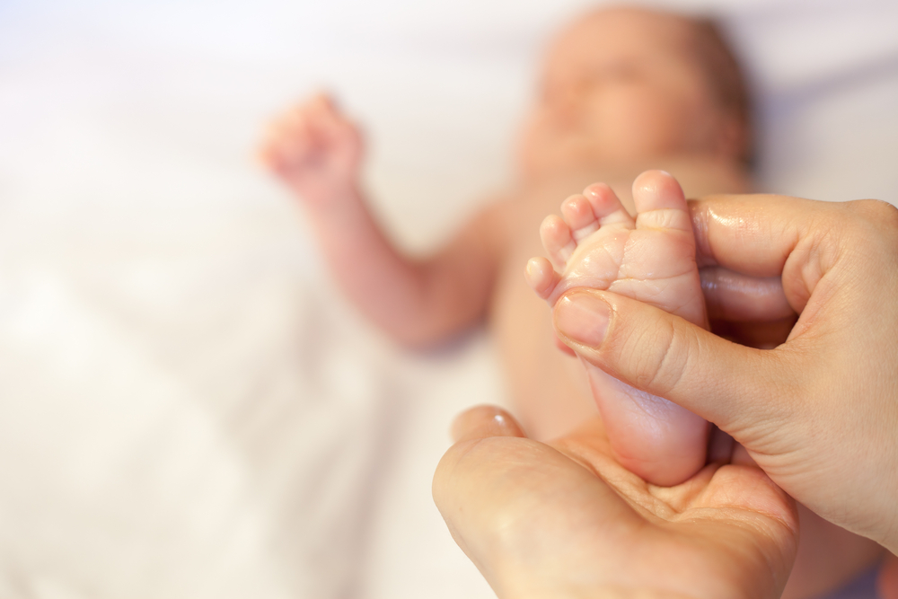 Botol minyak telon sedang disapu pada kaki bayi oleh ibu