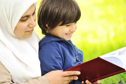 Ibu bertudung sedang mendengar bacaan bersama anak lelakinya di atas sofa