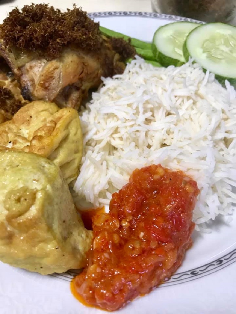 Gambar hidangan nasi ayam penyet lengkap dengan ayam goreng berempah, tahu, tempe, ulam dan sambal.
