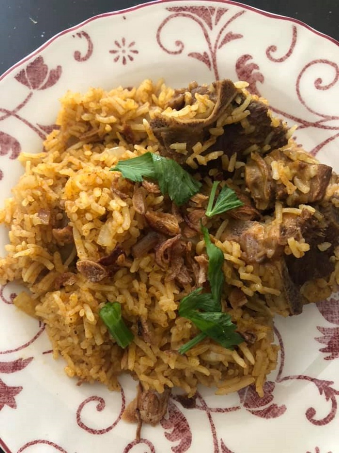 Sebuah mangkuk berisi nasi kari kambing yang siap dimasak dengan rempah dan daging kambing.