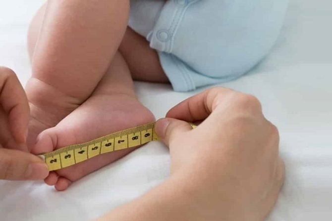 Ibu mengukur tapak kaki anak menggunakan pita pengukur
