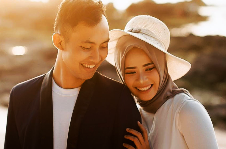 Pasangan suami isteri sedang duduk bergurau sambil ketawa dalam keadaan romantik.