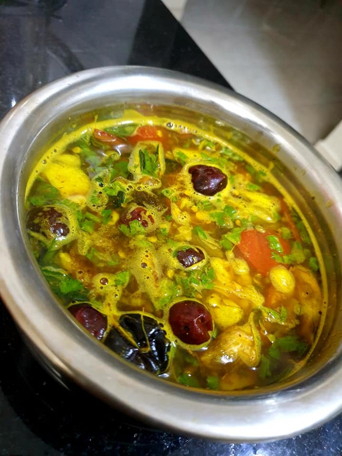 Sebuah mangkuk berisi hidangan rasam berkuah berwarna keperangan dengan hiasan daun ketumbar.