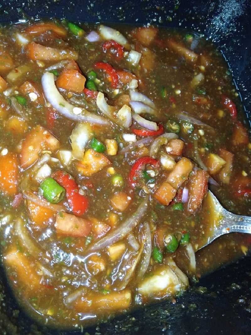 Mangkuk berisi air asam ikan bakar yang merah dengan cili dan tomato dipotong.