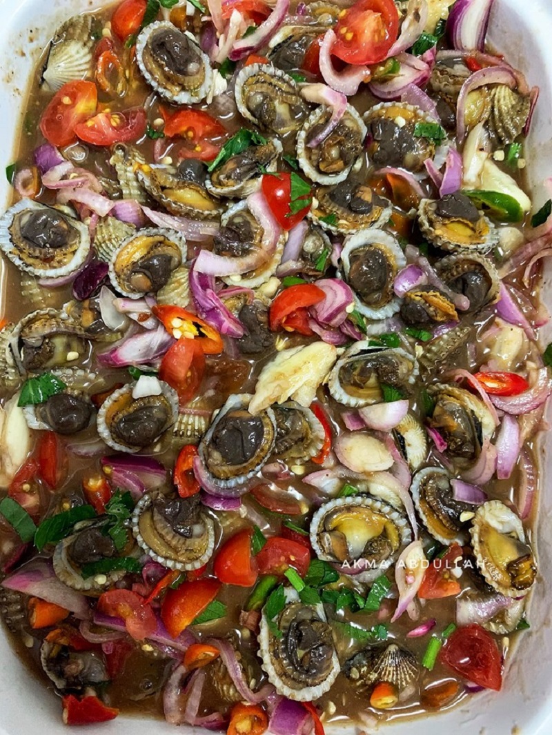 Mangkuk berisi kerang rebus dengan campuran air asam jawa, cili, tomato dan daun ketumbar.
