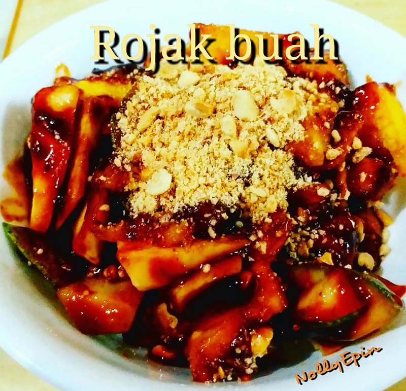 Mangkuk berisi kuah rojak buah berwarna gelap dengan taburan kacang tanah.