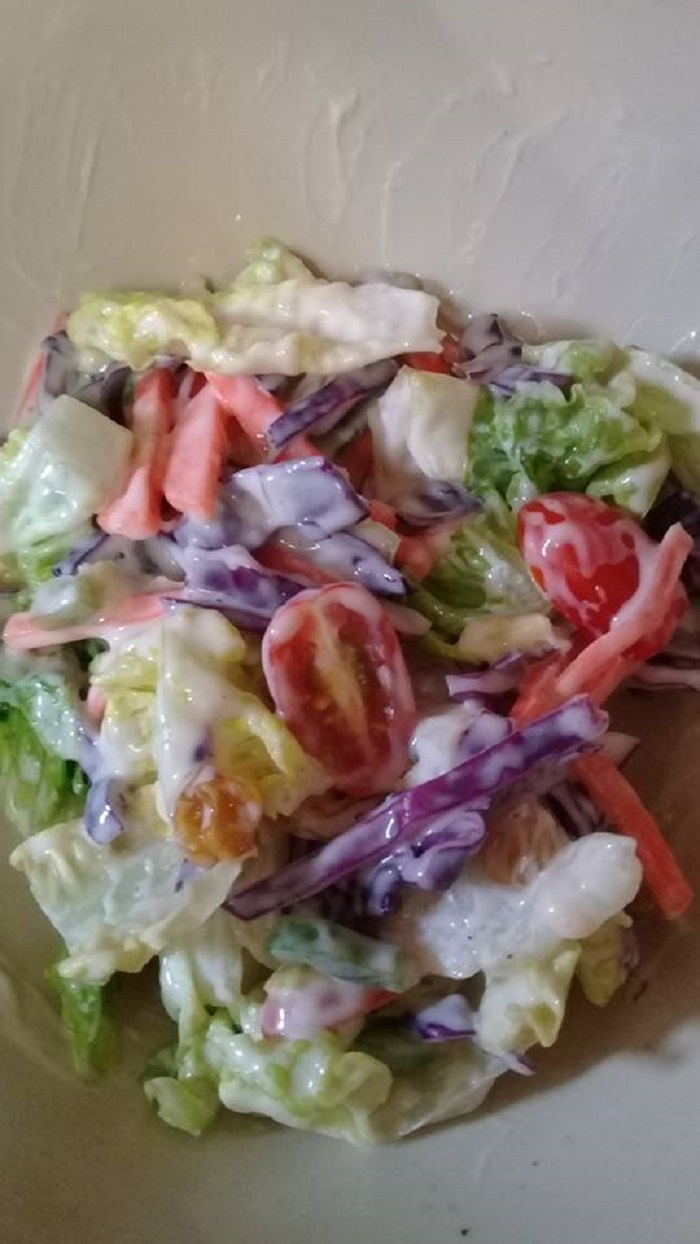 Semangkuk salad sayur segar dengan mayonis, kekacang dan kismis.
