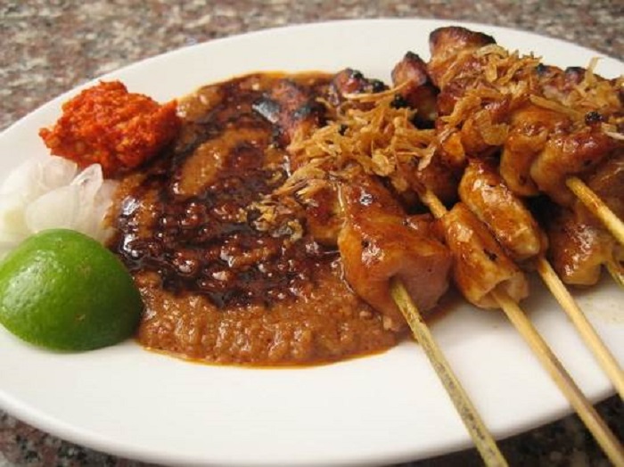 Gambar beberapa cucuk satay ayam yang dibakar berserta kuah kacang di dalam mangkuk kecil.
