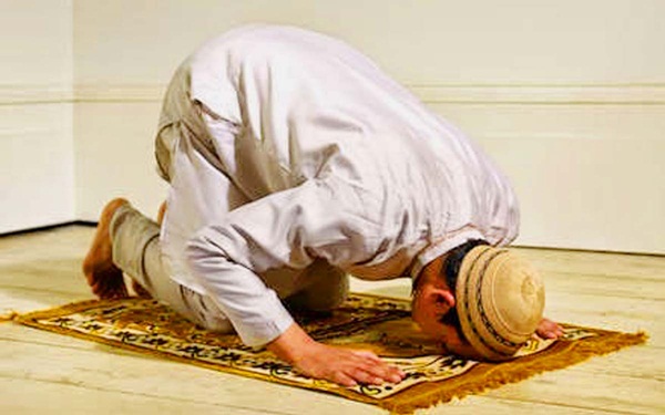 Lelaki muslim sedang menunaikan solat dengan telekung putih membulatkan tangan.