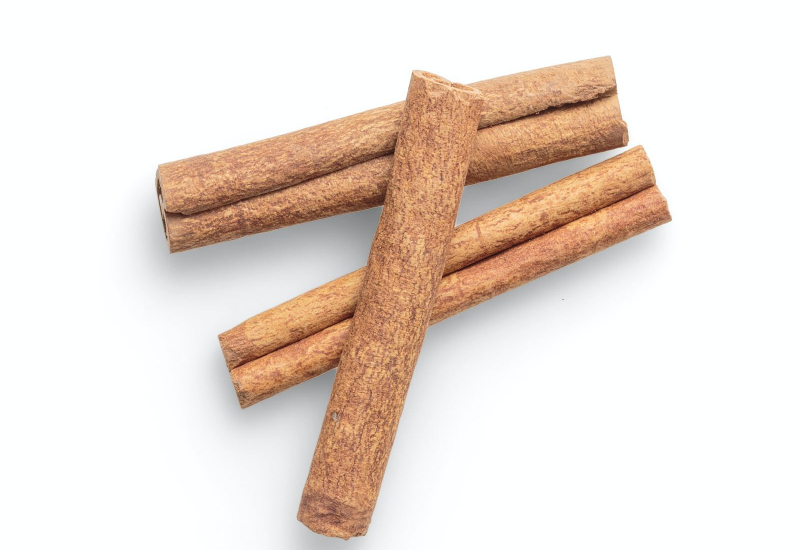 Serbuk kayu manis dan beberapa kayu manis di atas meja kayu.