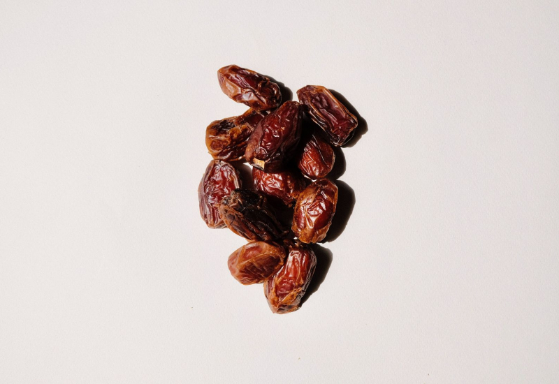 Pelbagai jenis buah kurma yang dipamerkan bersama daun palma sebagai latar belakang.