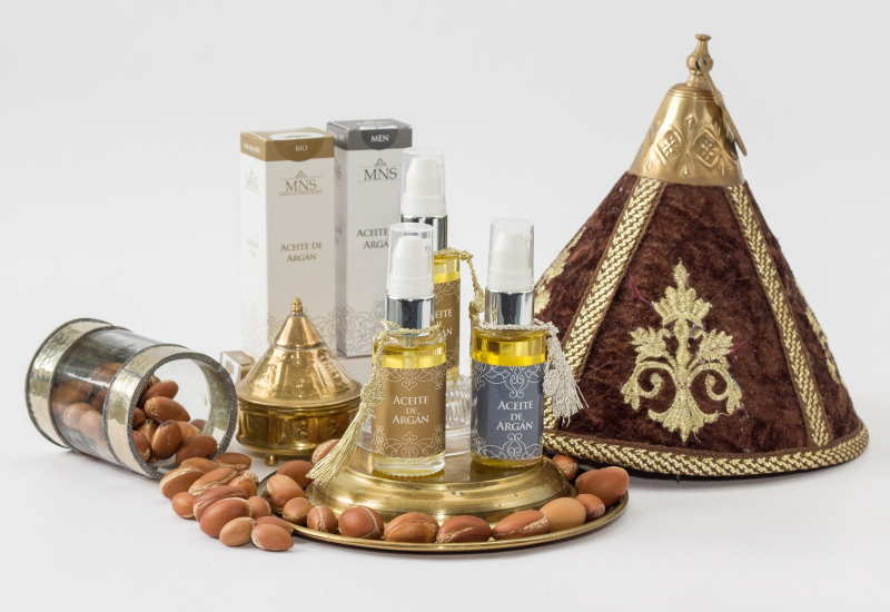 Botol kecil berisi minyak argan dikelilingi buah dan daun pokok argan