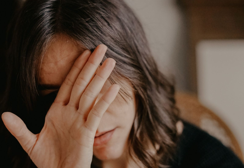Wanita menunjukkan tanda kurang keyakinan diri dengan tangan di muka