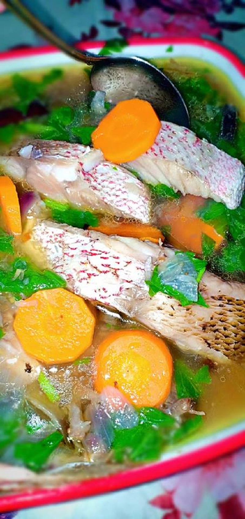 Sebuah mangkuk berisi sup ikan merah yang sedap bersama hirisan lobak merah dan daun sup.
