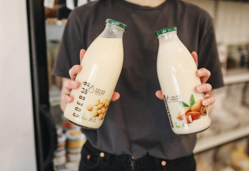 Segelas susu badam segar dengan bijirin oat dan kacang badam di sebelahnya