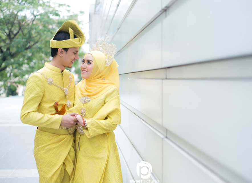 Gambar pasangan pengantin Melayu berpakaian majlis bersanding dengan pakaian warna yang menyeri.