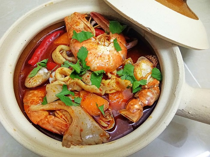 Semangkuk tomyam seafood pedas masam dengan udang, sotong dan cendawan.