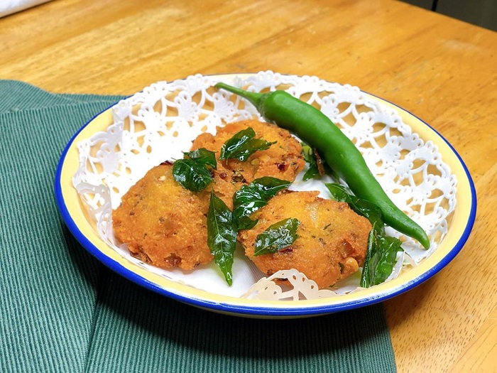 Sekeping vadai dal yang telah digoreng berwarna keperangan dengan hirisan cili dan daun kari.